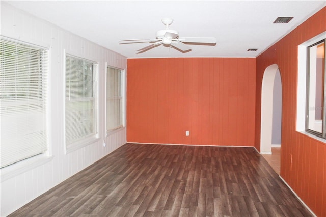 unfurnished room with ceiling fan, wooden walls, and dark hardwood / wood-style floors