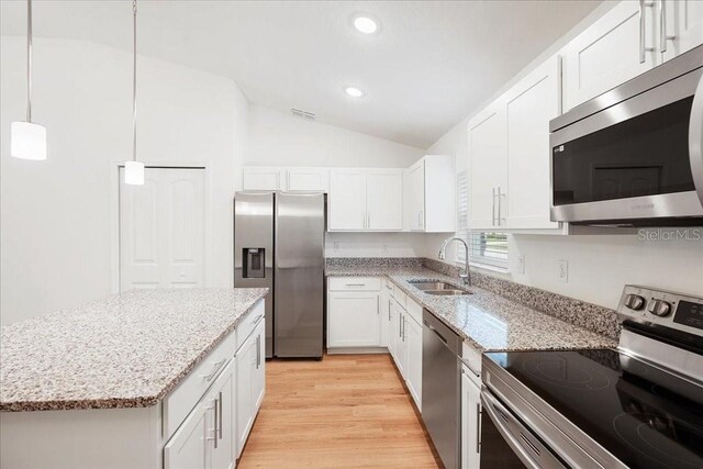 kitchen with lofted ceiling, white cabinets, sink, appliances with stainless steel finishes, and decorative light fixtures