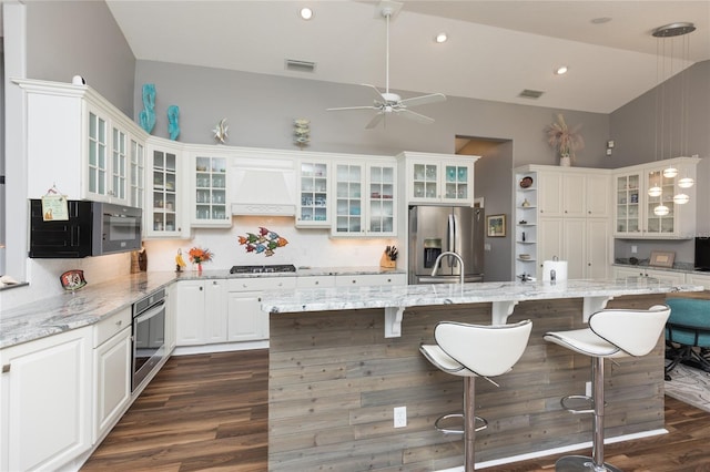 kitchen featuring light stone counters, a breakfast bar area, white cabinets, custom range hood, and appliances with stainless steel finishes