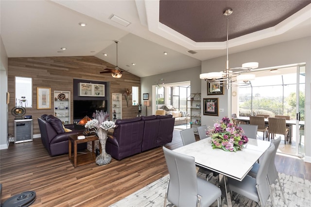 dining area with wood-type flooring, ceiling fan with notable chandelier, and wooden walls