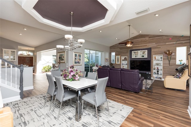 dining space featuring wood walls, hardwood / wood-style floors, and ceiling fan with notable chandelier