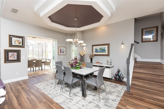 dining space featuring wood-type flooring, a raised ceiling, and a notable chandelier