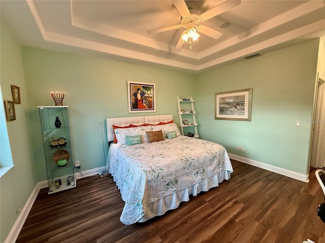 bedroom with a raised ceiling, ceiling fan, and dark wood-type flooring