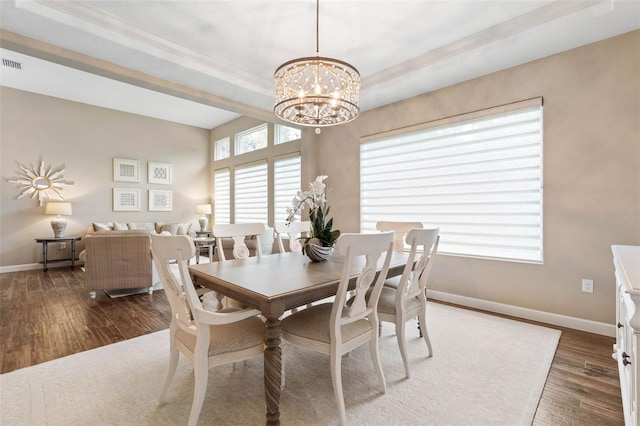 dining space with dark hardwood / wood-style floors, a raised ceiling, and a notable chandelier