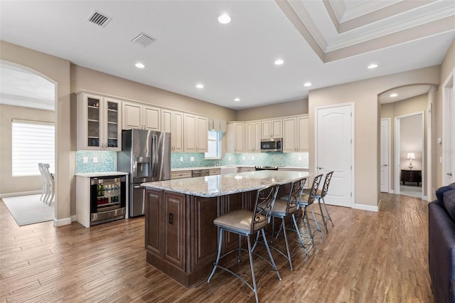 kitchen featuring a kitchen breakfast bar, stainless steel appliances, wood-type flooring, a center island, and wine cooler