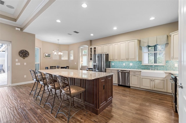 kitchen with appliances with stainless steel finishes, backsplash, sink, pendant lighting, and a center island