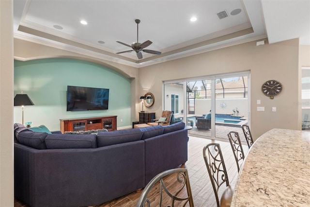 living room with a tray ceiling, ceiling fan, hardwood / wood-style floors, and ornamental molding