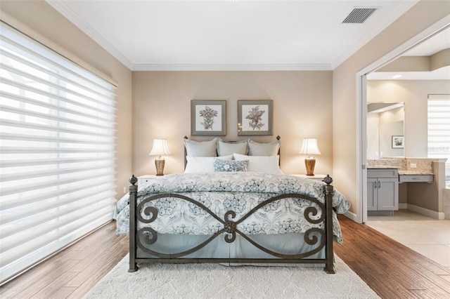 bedroom with ensuite bath, crown molding, and light wood-type flooring