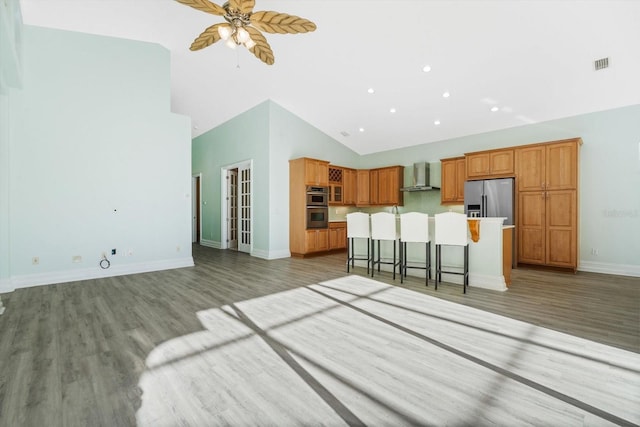 kitchen with wall chimney exhaust hood, stainless steel appliances, high vaulted ceiling, a center island, and a breakfast bar area