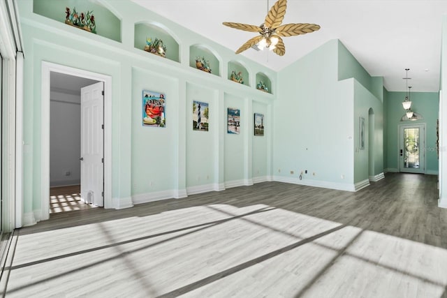 unfurnished room featuring built in shelves, ceiling fan, a high ceiling, and hardwood / wood-style flooring