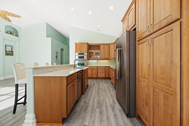 kitchen with stainless steel appliances, a kitchen bar, decorative backsplash, a center island with sink, and light wood-type flooring