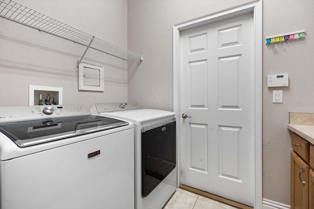 washroom featuring washing machine and clothes dryer, light tile patterned floors, and cabinets