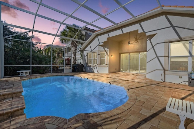 pool at dusk with glass enclosure, ceiling fan, and a patio area