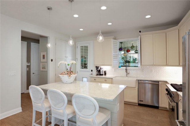 kitchen featuring light wood-type flooring, stainless steel appliances, sink, decorative light fixtures, and a center island