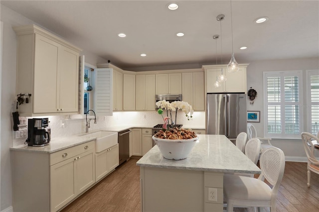 kitchen featuring sink, light hardwood / wood-style flooring, pendant lighting, a kitchen island, and appliances with stainless steel finishes