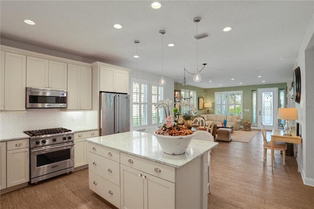 kitchen with light stone countertops, high end appliances, pendant lighting, a center island, and light hardwood / wood-style floors