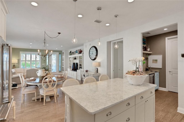 kitchen with decorative light fixtures, light hardwood / wood-style flooring, a notable chandelier, a kitchen island, and white cabinetry