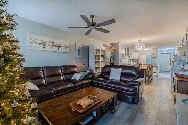 living room featuring ceiling fan with notable chandelier, wood-type flooring, and a textured ceiling