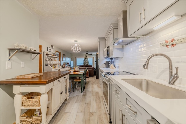 kitchen featuring stainless steel range with electric stovetop, backsplash, sink, a textured ceiling, and butcher block counters