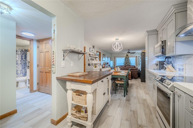 kitchen featuring wood counters, appliances with stainless steel finishes, decorative backsplash, wall chimney range hood, and light hardwood / wood-style flooring