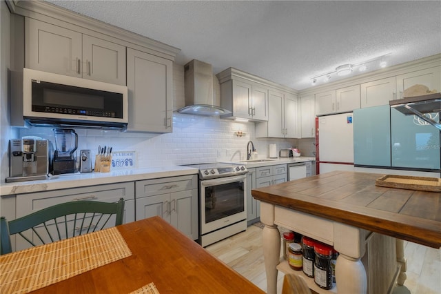 kitchen with wall chimney range hood, light hardwood / wood-style flooring, electric range, a textured ceiling, and white fridge