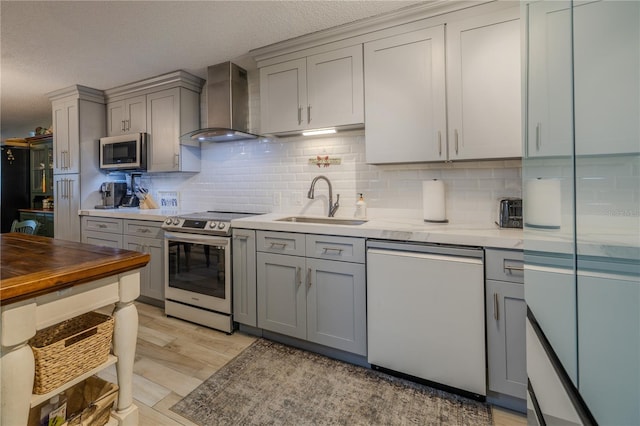 kitchen featuring appliances with stainless steel finishes, wall chimney exhaust hood, a textured ceiling, sink, and light hardwood / wood-style floors