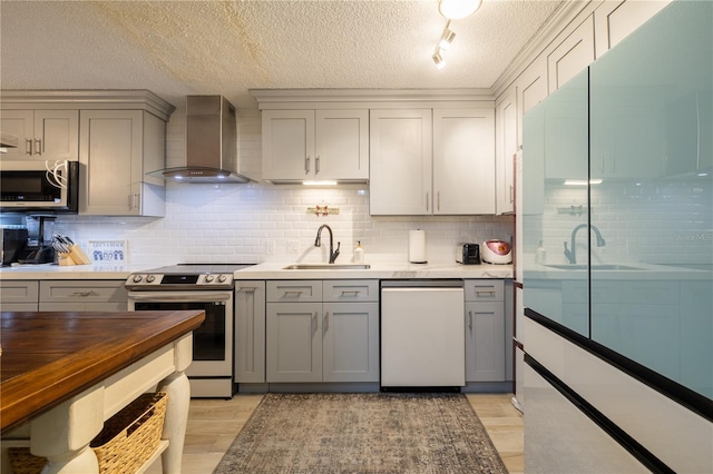 kitchen featuring gray cabinetry, sink, wall chimney range hood, a textured ceiling, and appliances with stainless steel finishes