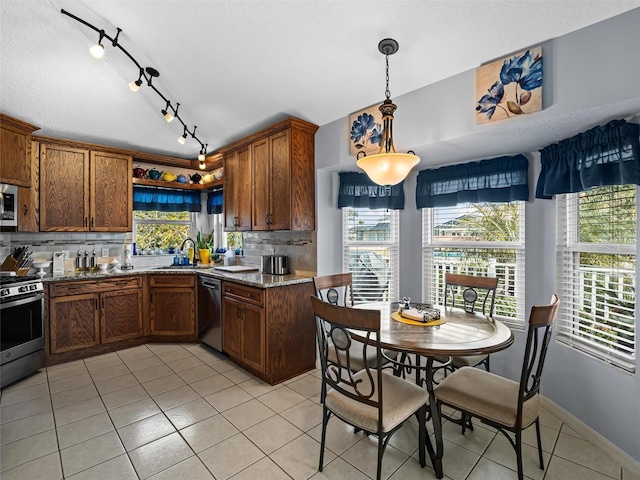 kitchen with appliances with stainless steel finishes, tasteful backsplash, light stone counters, light tile patterned floors, and hanging light fixtures