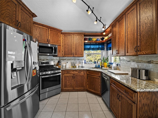 kitchen featuring sink, light tile patterned floors, a textured ceiling, light stone counters, and stainless steel appliances