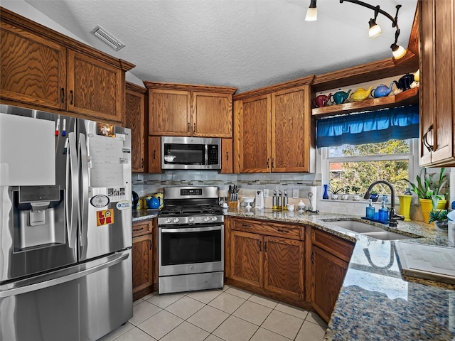 kitchen featuring sink, light tile patterned floors, a textured ceiling, light stone counters, and stainless steel appliances