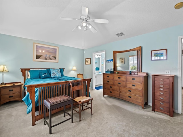 bedroom with a textured ceiling, ceiling fan, light carpet, and connected bathroom