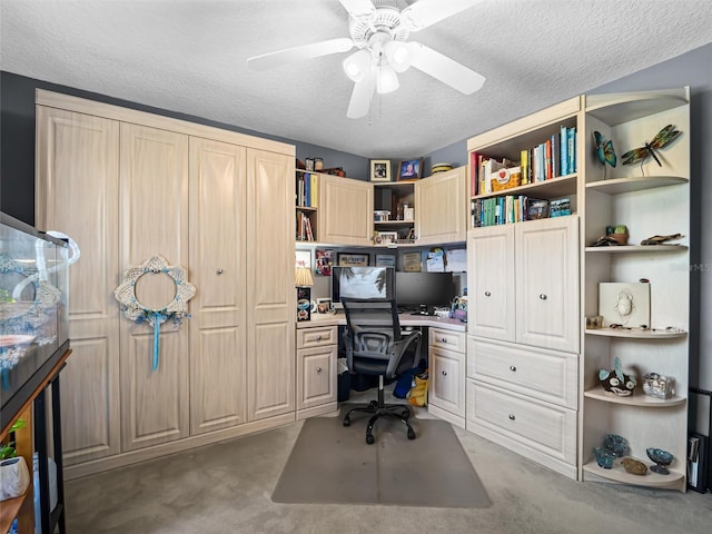 office space featuring ceiling fan, light colored carpet, built in desk, and a textured ceiling