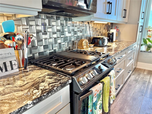 kitchen featuring high end range, backsplash, dark stone counters, dark wood-type flooring, and white cabinets