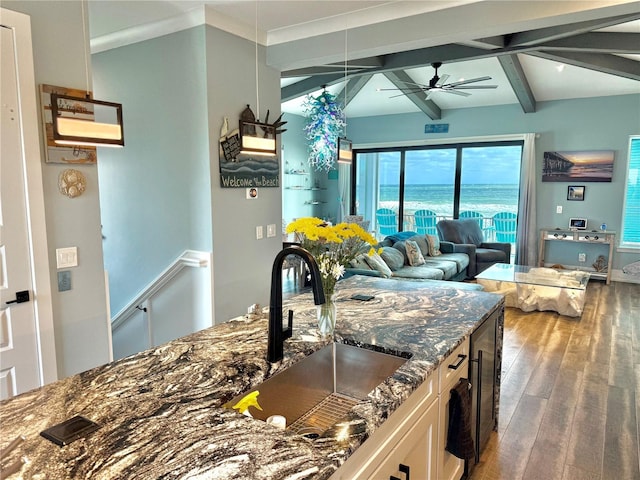 kitchen with white cabinets, a water view, sink, dark stone countertops, and beam ceiling