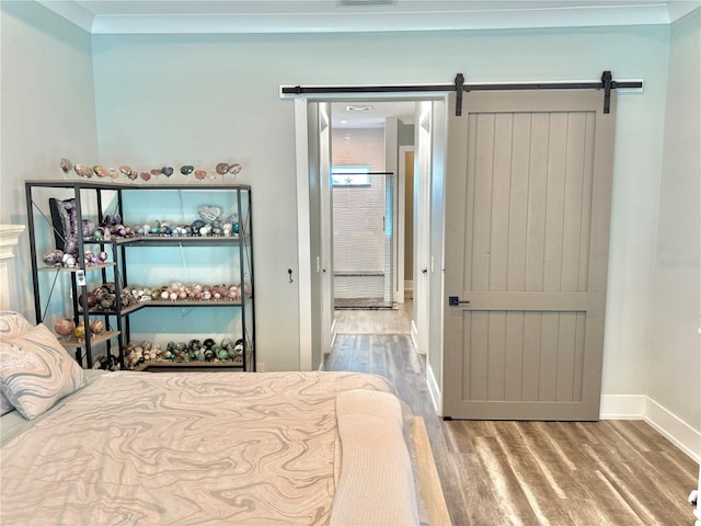 bedroom featuring a barn door, hardwood / wood-style flooring, and crown molding