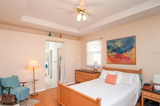 bedroom with ceiling fan, a tray ceiling, and light wood-type flooring