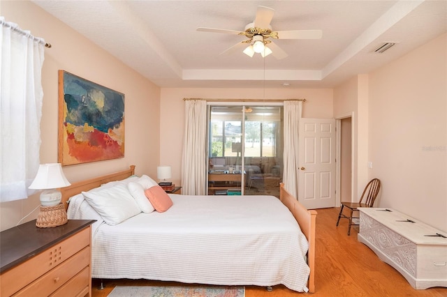 bedroom featuring ceiling fan, wood-type flooring, a tray ceiling, and access to outside