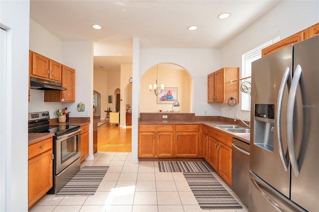 kitchen featuring light tile patterned floors, arched walkways, a sink, stainless steel appliances, and under cabinet range hood