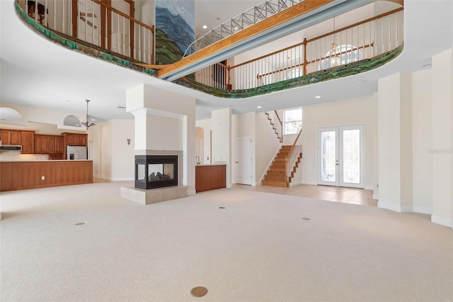 unfurnished living room with light colored carpet, french doors, a towering ceiling, and a fireplace