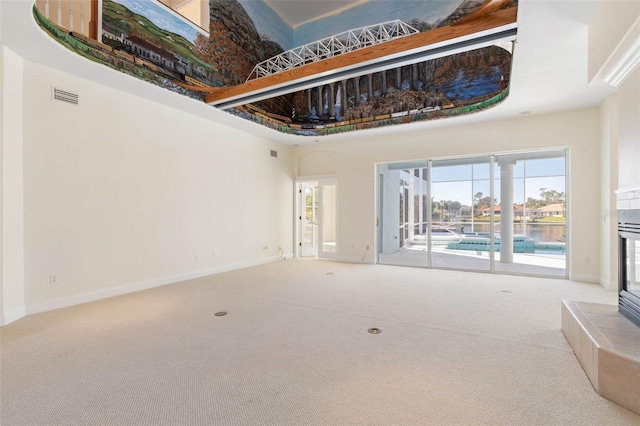 unfurnished living room with a high ceiling, a tile fireplace, and carpet flooring