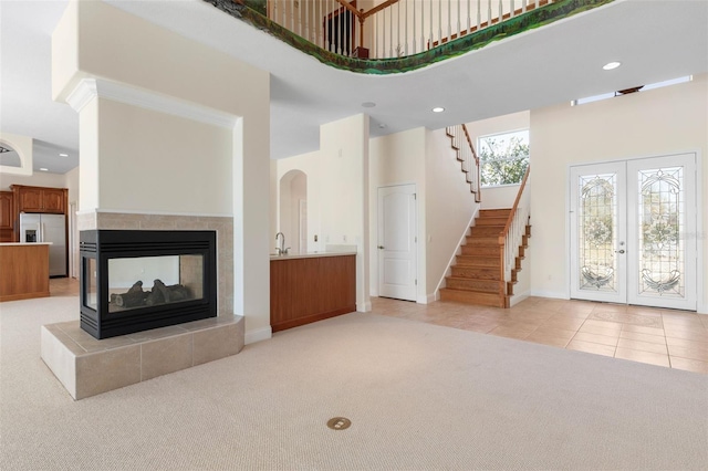 carpeted living room with a towering ceiling, sink, french doors, and a tiled fireplace