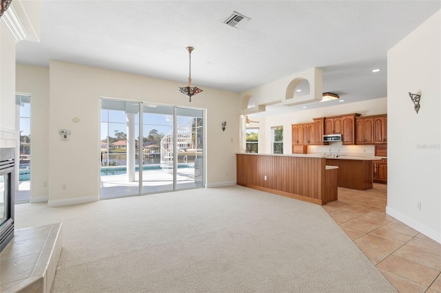 kitchen featuring hanging light fixtures, light colored carpet, kitchen peninsula, and a tile fireplace