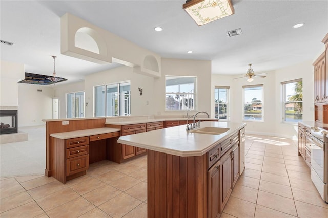 kitchen featuring a center island with sink, ceiling fan, a multi sided fireplace, light colored carpet, and sink