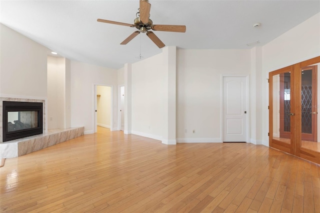 unfurnished living room featuring a multi sided fireplace, french doors, ceiling fan, and light wood-type flooring