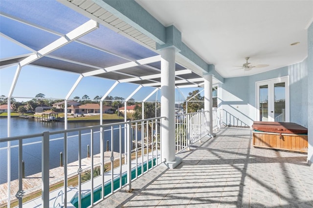 view of patio / terrace with a lanai, a hot tub, ceiling fan, french doors, and a water view