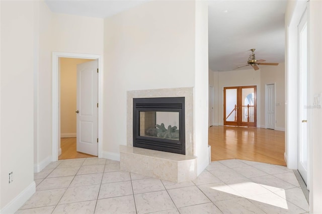 unfurnished living room featuring ceiling fan, light tile patterned floors, and a high end fireplace