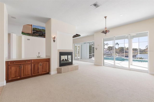 unfurnished living room with light carpet, a water view, a fireplace, and sink