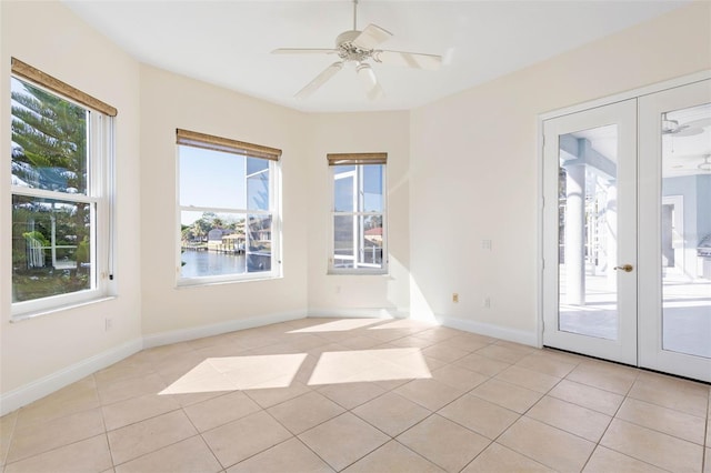 empty room featuring ceiling fan, a water view, french doors, and light tile patterned flooring