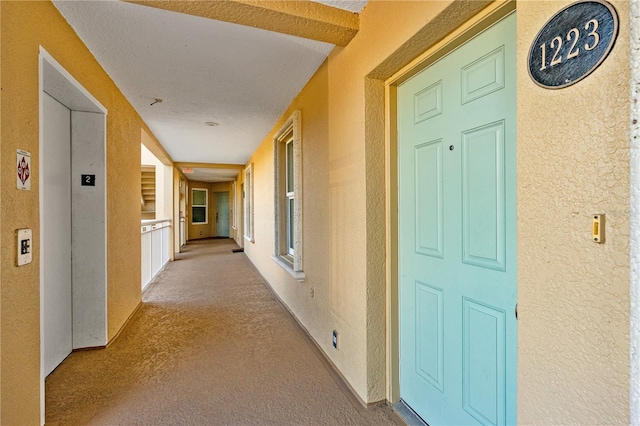 hallway featuring elevator and light colored carpet