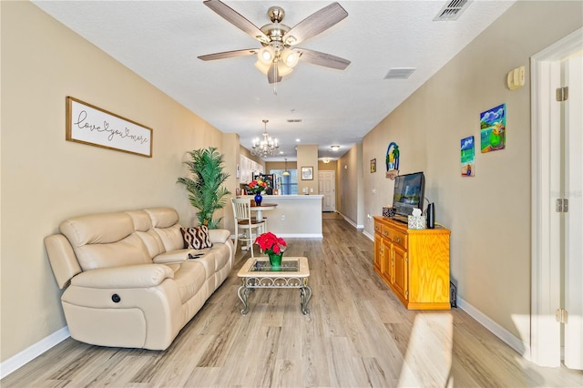 living room featuring ceiling fan with notable chandelier, light hardwood / wood-style floors, and a textured ceiling